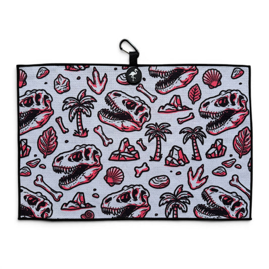 Logie Joe’s Fossil microfiber golf towel laid flat, showing dinosaur skulls, fossils, palm trees and a carabiner